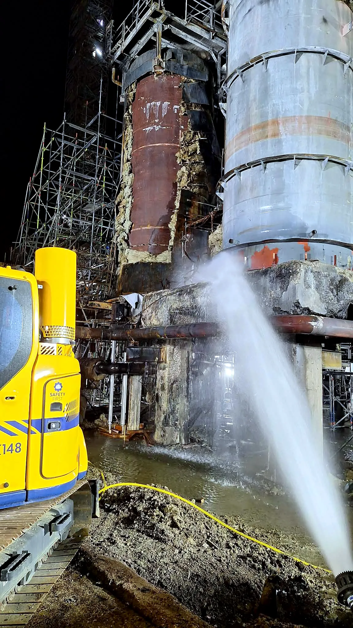 Nocna rozbiórka instalacji zakładu chemicznego: koparka i zraszanie pyłu